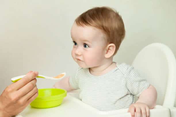 Bébé l'air étonné en train de manger son repas sur une chaise haute